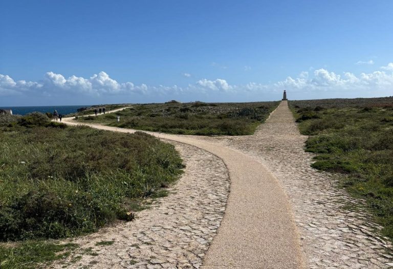 ein Weg wird zu zwei Wegen, einer verläuft Richtung Meer, der andere führt zu einem Leuchtturm am Horizont 