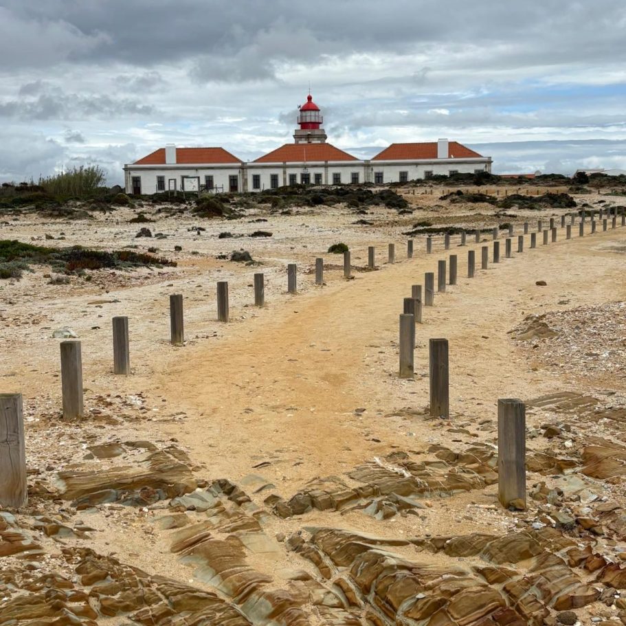 mit Holzpflöcken gefasster Sandweg, der zu Leuchtturmgebäudekomplex leitet, Steilküstenlanschaft, bewölkter Himmel